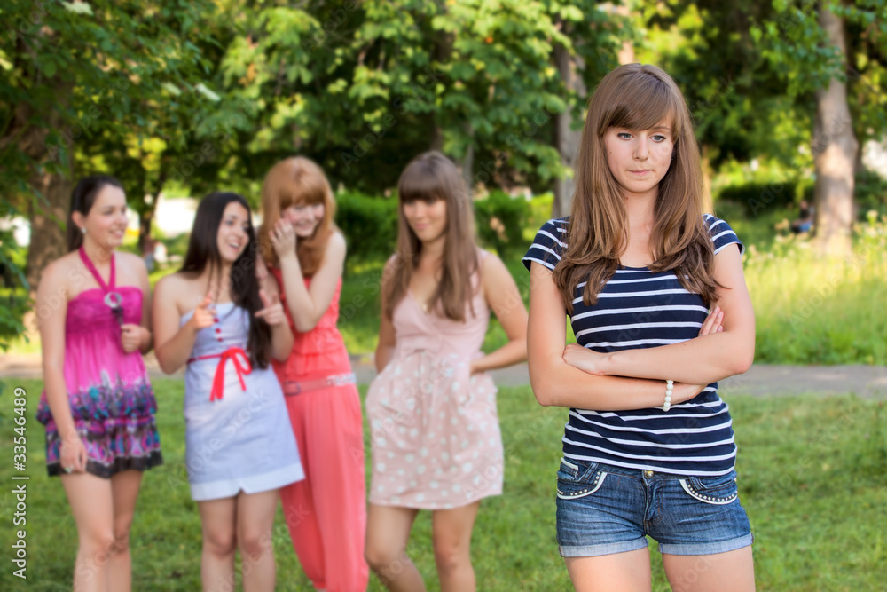 Upset teenage girl with friends gossiping in park Upset teenage girl with friends gossiping in park