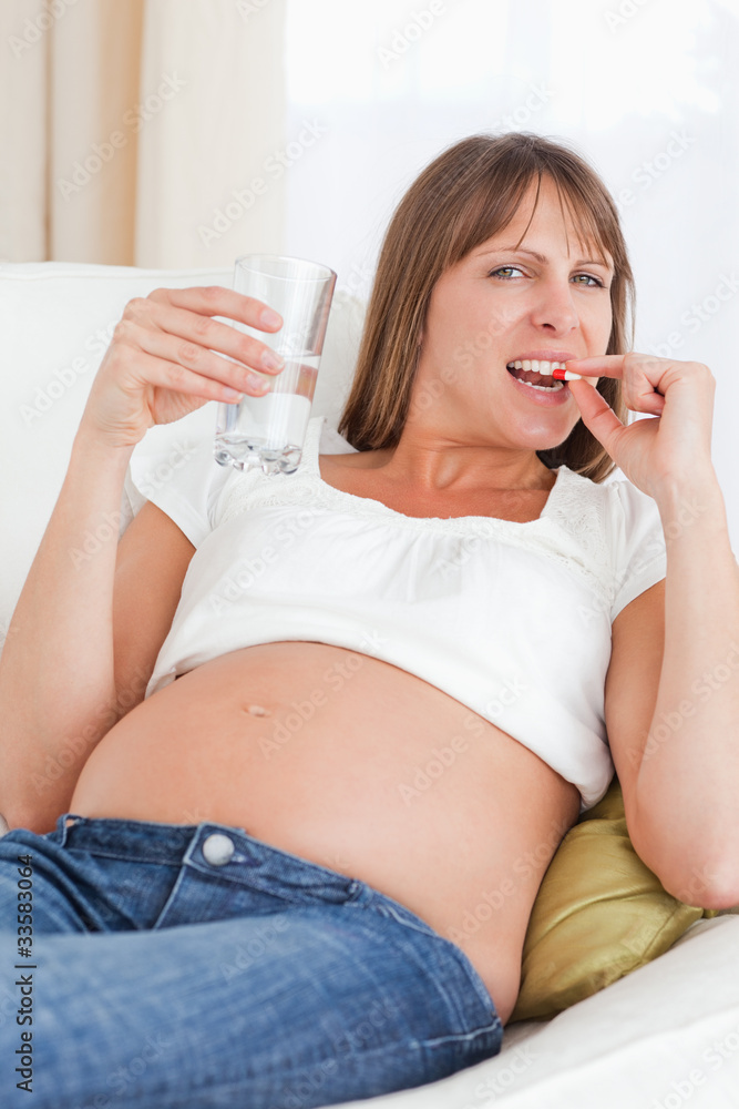 Good looking pregnant woman taking a pill while lying on a sofa Good looking pregnant woman taking a pill while lying on a sofa
