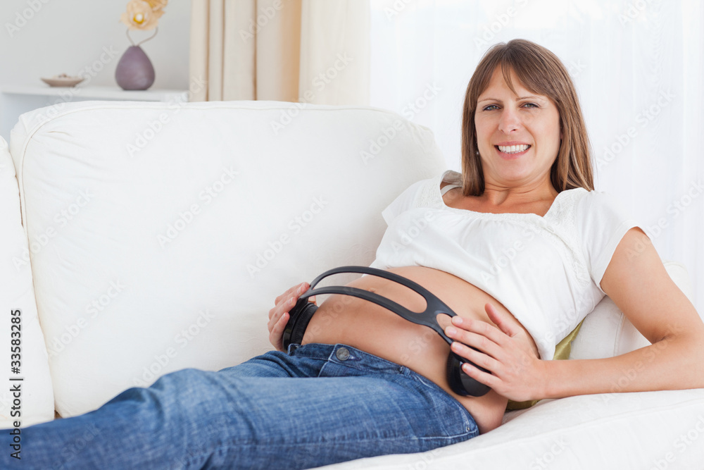 Smiling pregnant woman with headphones on her belly Smiling pregnant woman with headphones on her belly