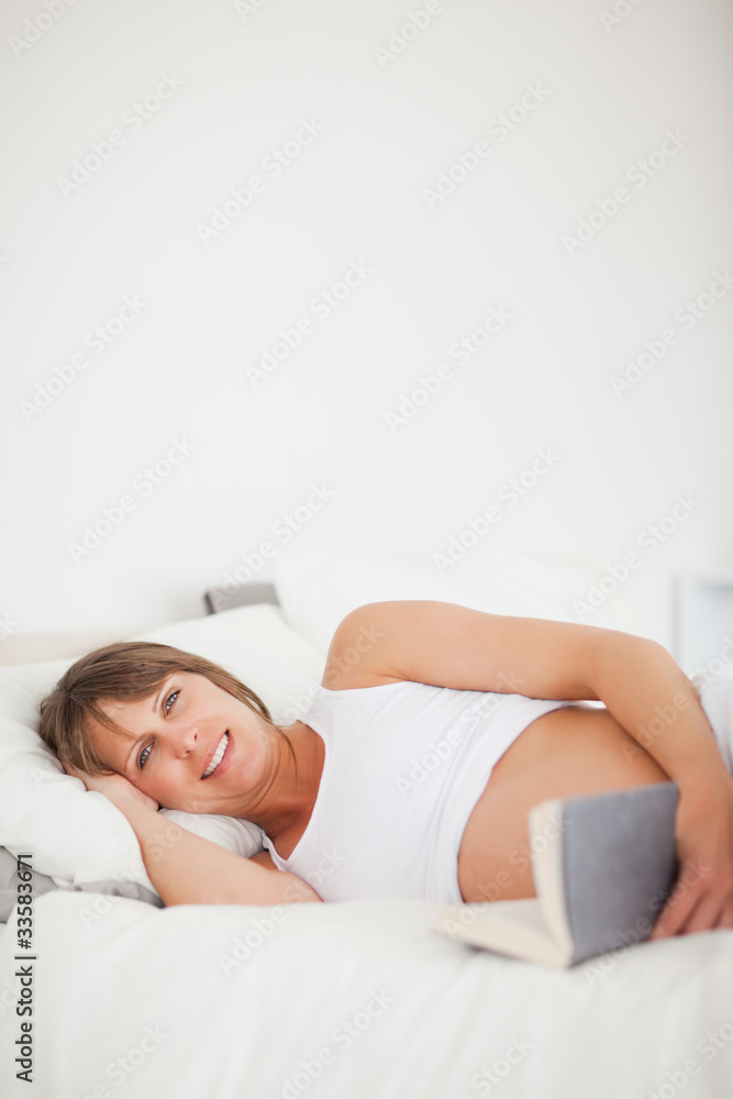 Charming pregnant woman reading a book while lying on her bed Charming pregnant woman reading a book while lying on her bed