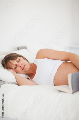 Good looking pregnant woman reading a book while lying on her be