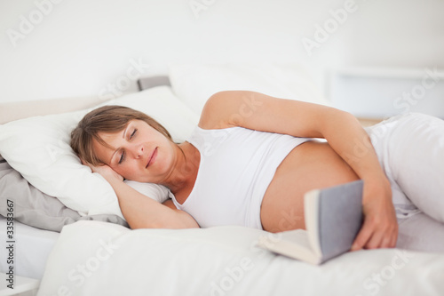 Beautiful pregnant woman reading a book while lying on her bed