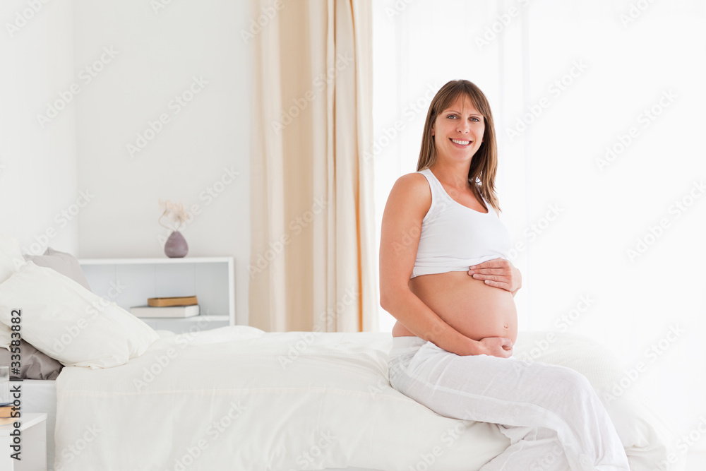 Beautiful pregnant female posing while sitting on a bed Beautiful pregnant female posing while sitting on a bed