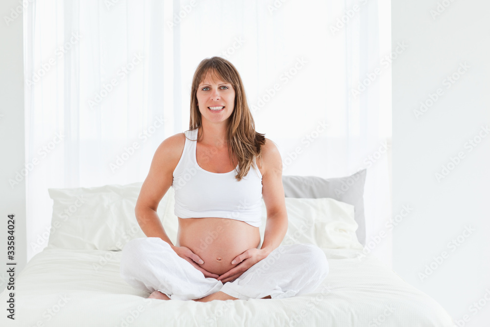 Good looking pregnant female posing while sitting on a bed Good looking pregnant female posing while sitting on a bed