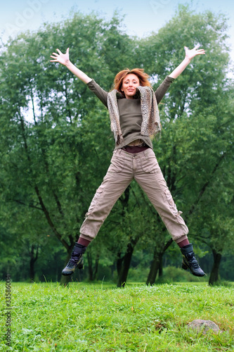 The girl jumps on a grass and trees as a background