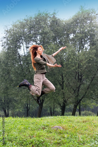The girl jumps on a grass and trees as a background