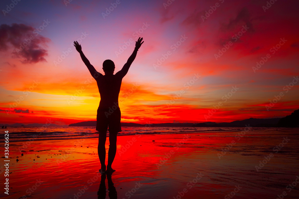 Young man standing with raised hands on a beach