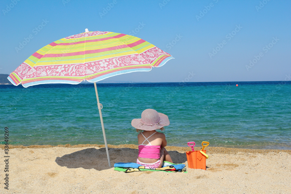 little girl sitting on beach under sunshade little girl sitting on beach under sunshade