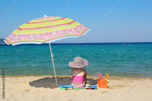 Wallpaper Mural little girl sitting on beach under sunshade Torontodigital.ca