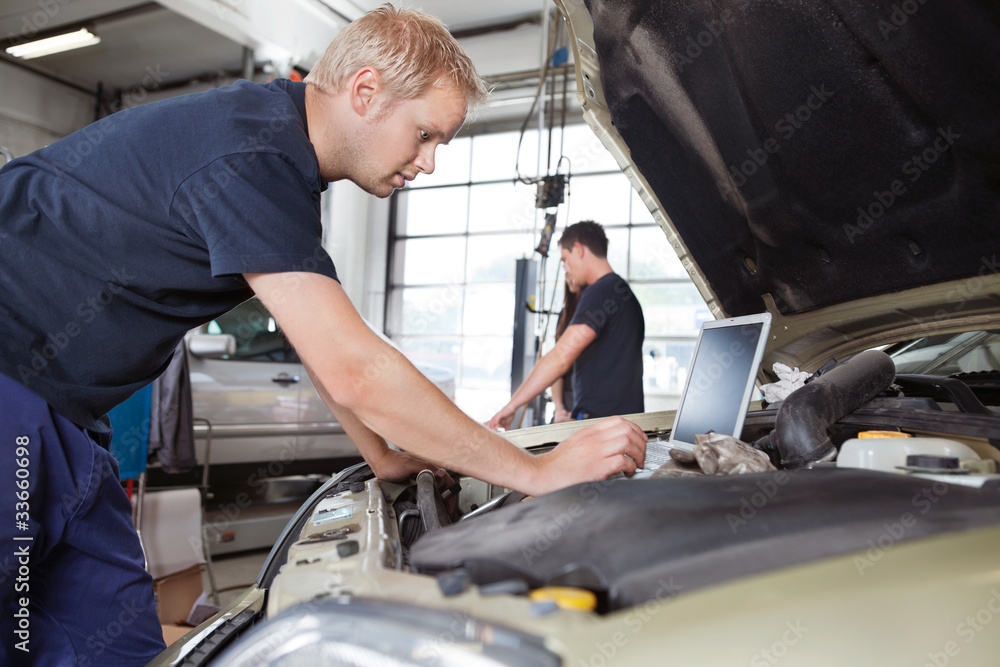 Mechanic using laptop while working on car Mechanic using laptop while working on car
