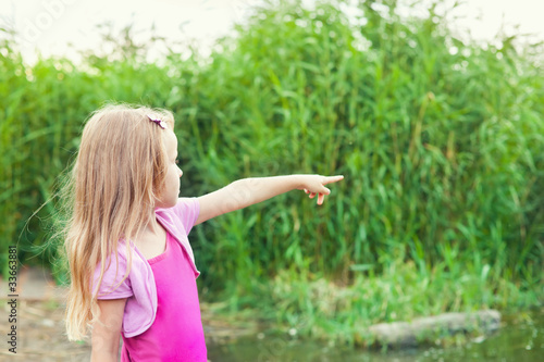 blonde little girl shows forefingers aside near river with canes