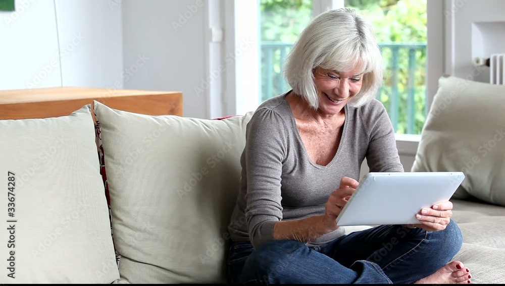 Senior woman sitting in sofa with electronic tablet Senior woman sitting in sofa with electronic tablet