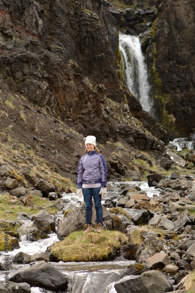 Frau steht vor einem natürlichen Wasserfall in Island Frau steht vor einem natürlichen Wasserfall in Island