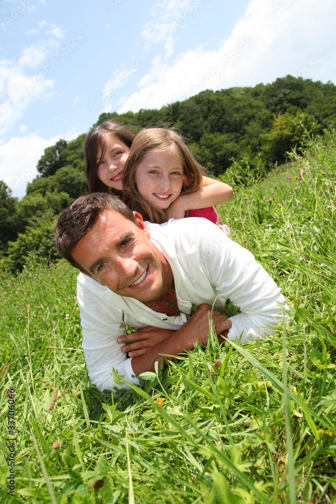 Fototapeta premium Man lying down in park with girls on his back