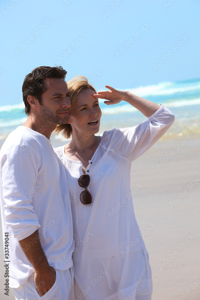 Couple stood on the beach wearing white clothing Couple stood on the beach wearing white clothing