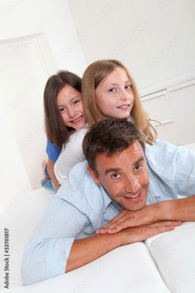 Fototapeta premium Man lying down on sofa with girls on his back