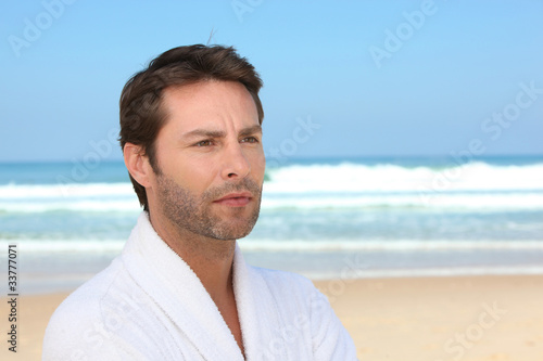 Distracted man standing on the beach in a bathrobe