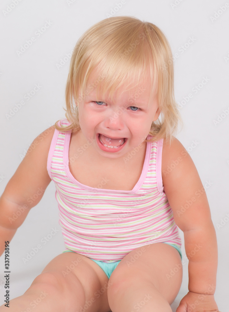 Adorable unsatisfied toddler girl sit and cry on white backgroun Adorable unsatisfied toddler girl sit and cry on white backgroun