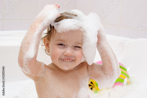 cute baby is washing her hair in bath