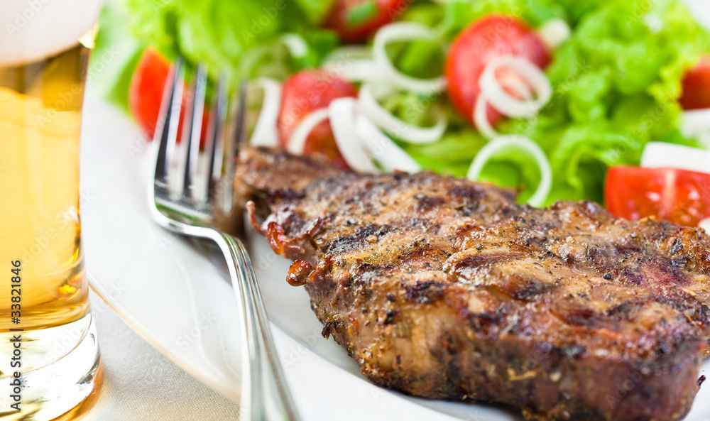 Grilled pork steak with salad and a glass of beer Grilled pork steak with salad and a glass of beer