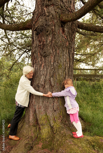Oma und Enkelin umarmen einen grossen Baum