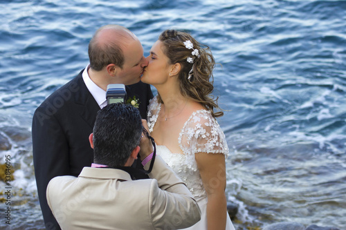 Fotografo con gli sposi che si baciano in riva al mare