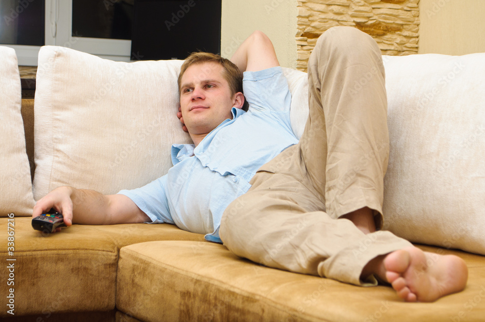 Man lying on sofa watching TV at home.
