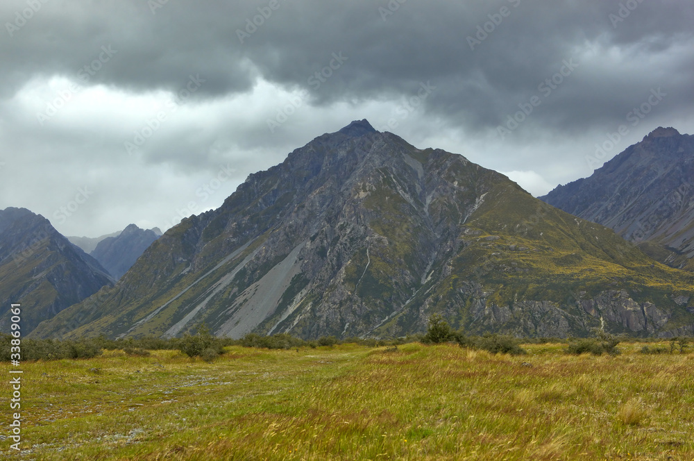 New Zealand hooker valley landscape mountain range scenery with green fields and dramatic grey skies.