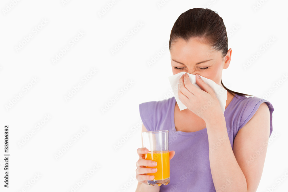 Good looking woman holding a glass of orange juice and sneezing Good looking woman holding a glass of orange juice and sneezing