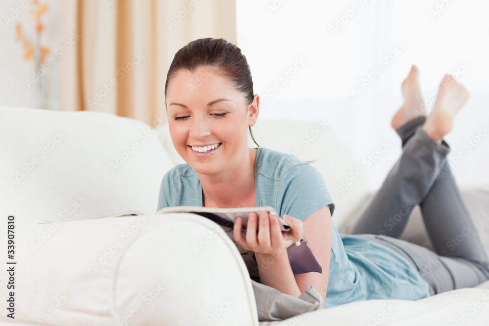 Lovely woman reading a magazine while lying on a sofa Lovely woman reading a magazine while lying on a sofa