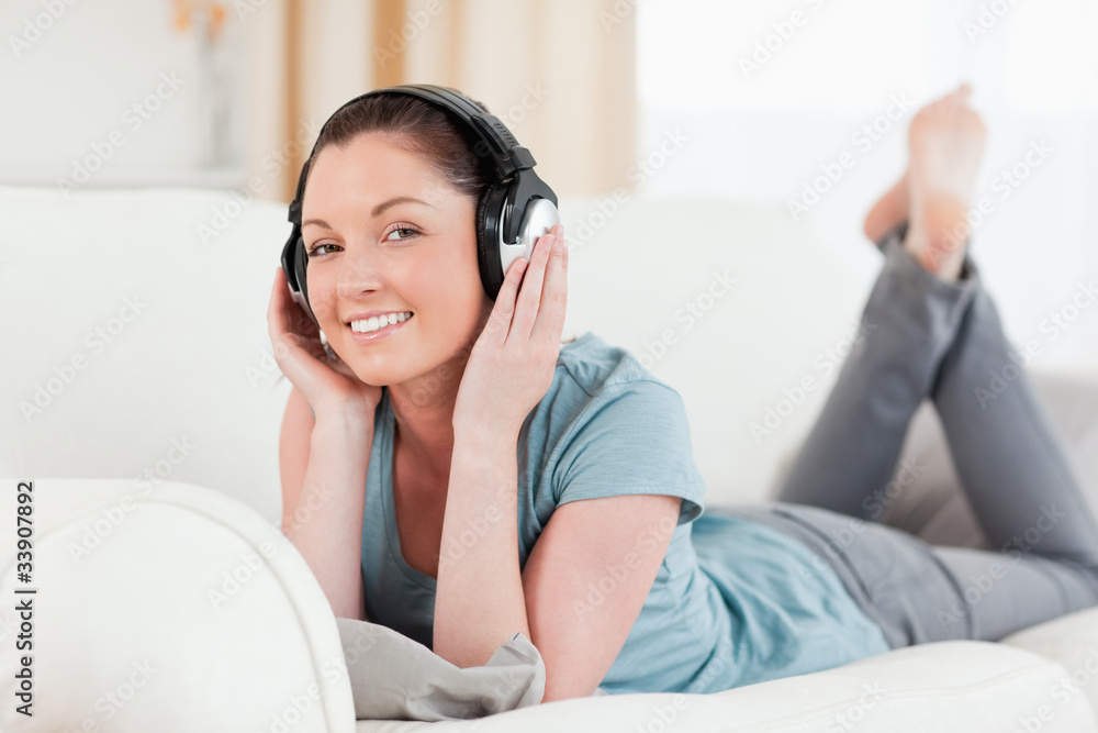 Charming woman with headphones posing while lying on a sofa Charming woman with headphones posing while lying on a sofa