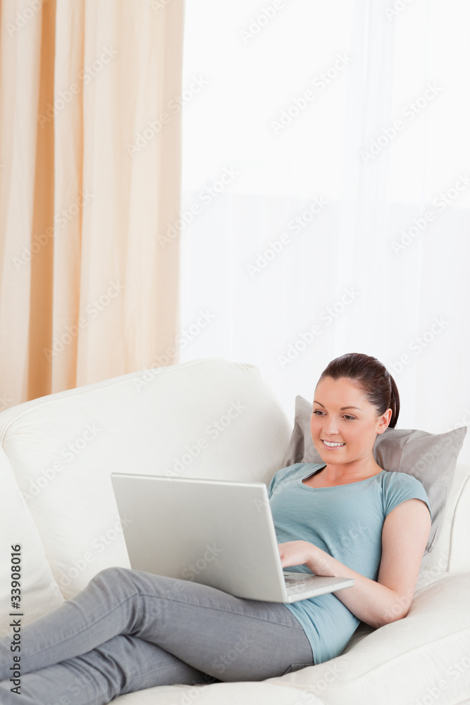 Cute woman relaxing with her laptop while lying on a sofa Cute woman relaxing with her laptop while lying on a sofa