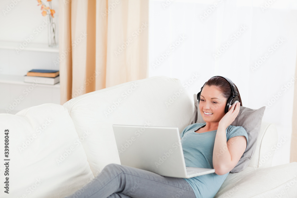 Beautiful female with headphones relaxing on her laptop while ly Beautiful female with headphones relaxing on her laptop while ly