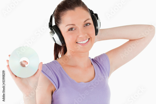 Charming woman with headphones holding a CD while standing