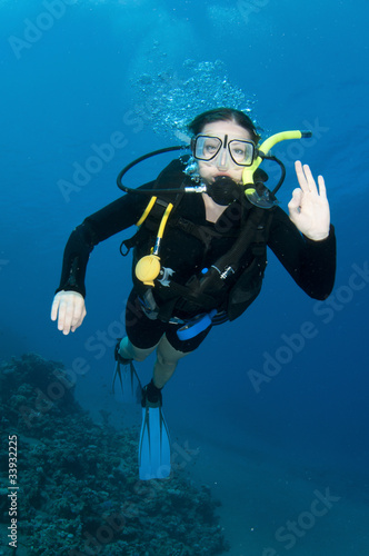 woman Scuba diver swims in clear blue ocean and makes OK sign
