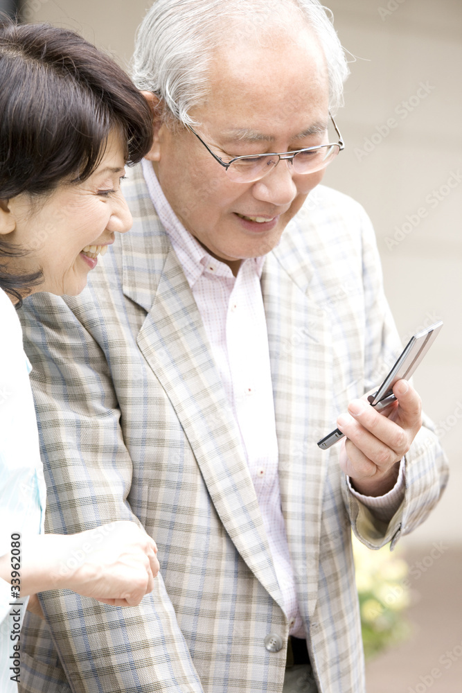 街中で携帯電話のメールを確認する老夫婦 街中で携帯電話のメールを確認する老夫婦