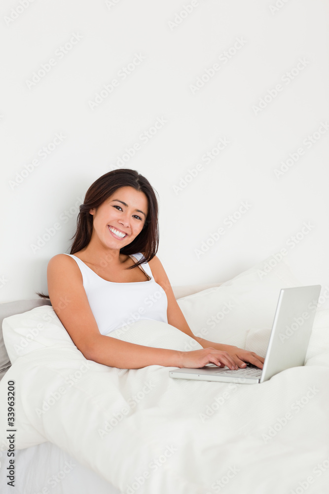 smiling woman with notebook lying in bed looking into camera smiling woman with notebook lying in bed looking into camera