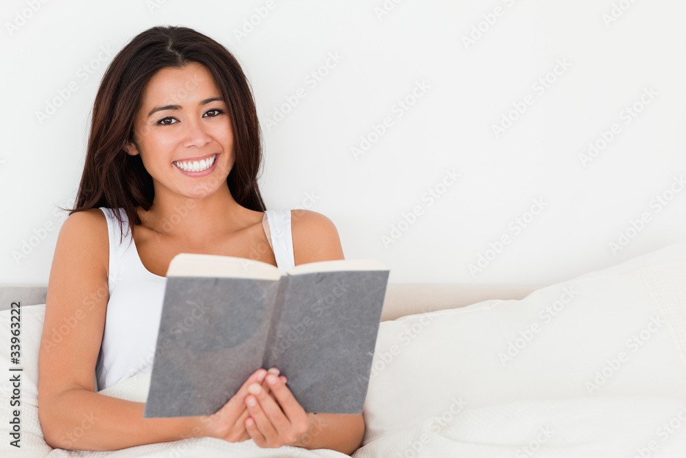 charming woman holding book lying in bed looking into camera charming woman holding book lying in bed looking into camera