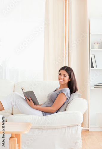 smiling woman lying on sofa holding a book