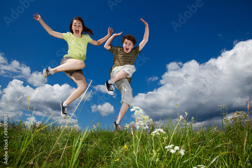 Girl and boy jumping, running against blue sky