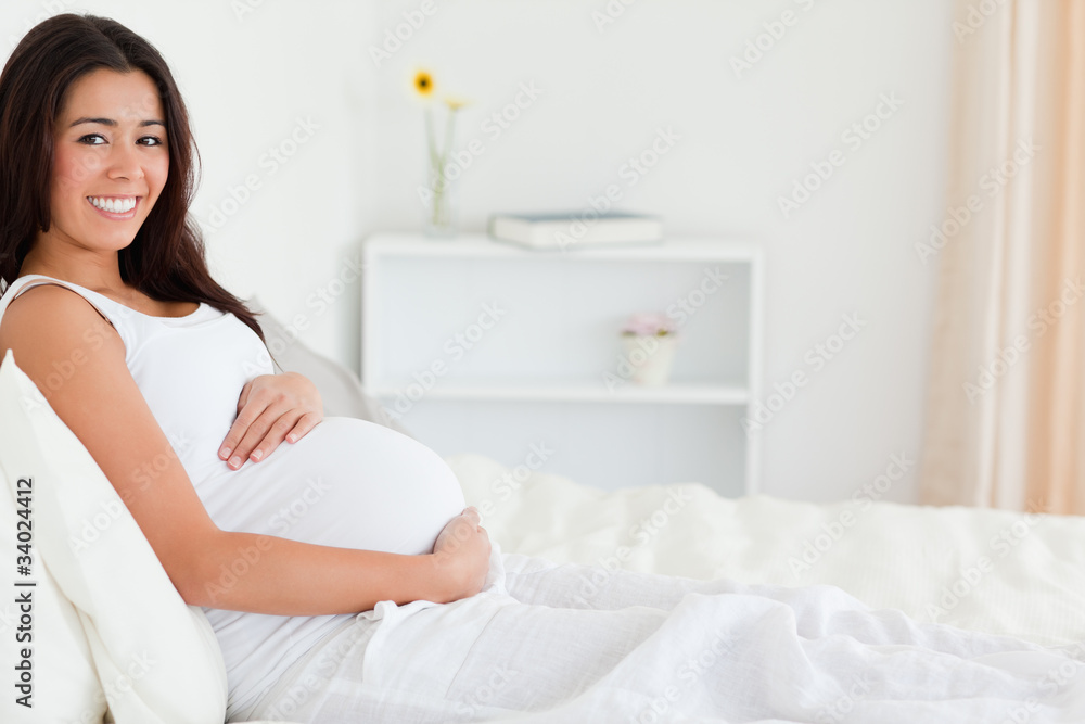 Good looking pregnant woman touching her belly while lying on a Good looking pregnant woman touching her belly while lying on a