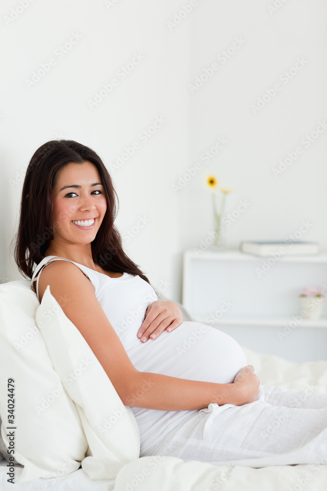 Pretty pregnant woman touching her belly while lying on a bed Pretty pregnant woman touching her belly while lying on a bed