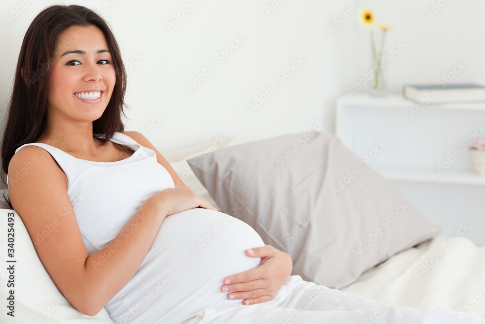Cute pregnant woman touching her belly while lying on a bed Cute pregnant woman touching her belly while lying on a bed