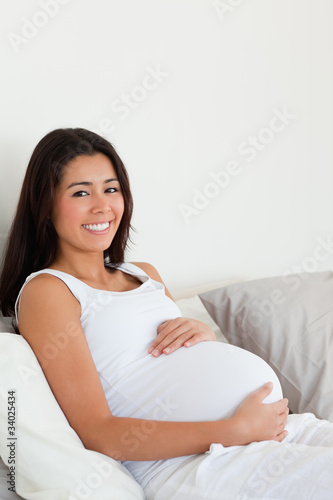 Lovely pregnant woman touching her belly while lying on a bed