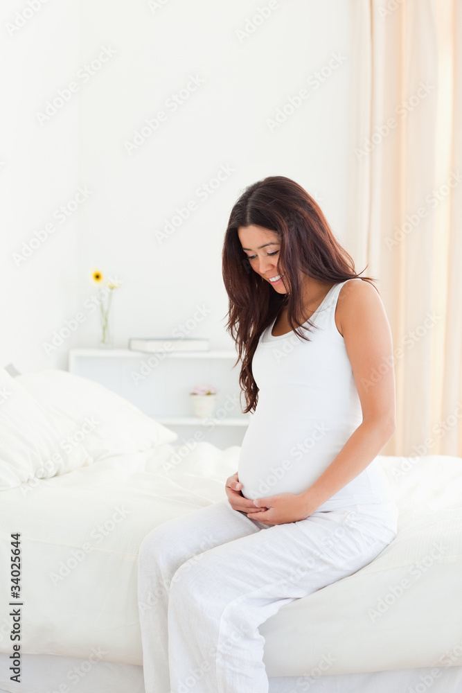 Good looking pregnant woman touching her belly while sitting on Good looking pregnant woman touching her belly while sitting on