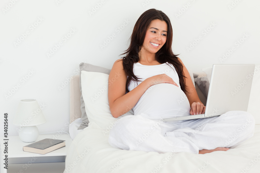 Beautiful pregnant woman relaxing with her laptop while lying on Beautiful pregnant woman relaxing with her laptop while lying on