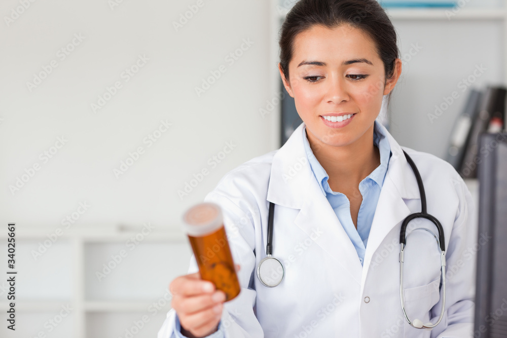 Beautiful smiling doctor holding and looking at a box of pills Beautiful smiling doctor holding and looking at a box of pills