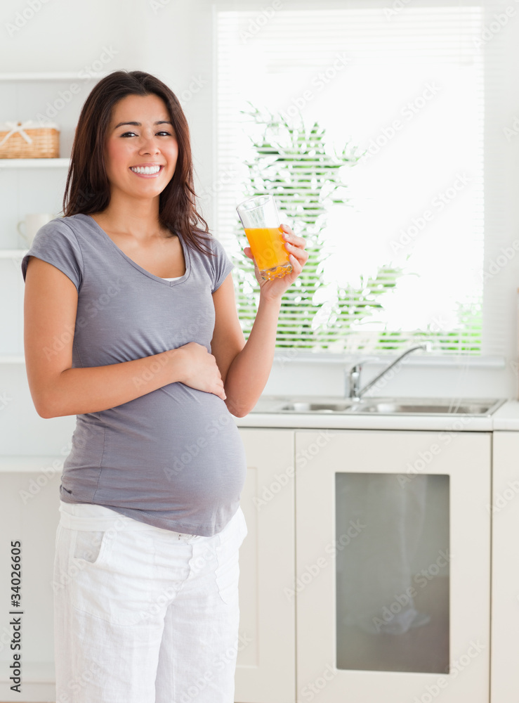Gorgeous pregnant woman holding a glass of orange juice while st Gorgeous pregnant woman holding a glass of orange juice while st