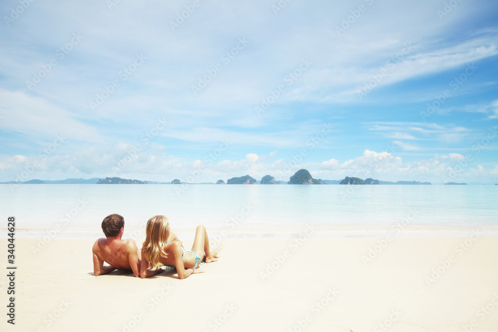 Young couple sitting on the sand and looking to a blue tropical sky Young couple sitting on the sand and looking to a blue tropical sky