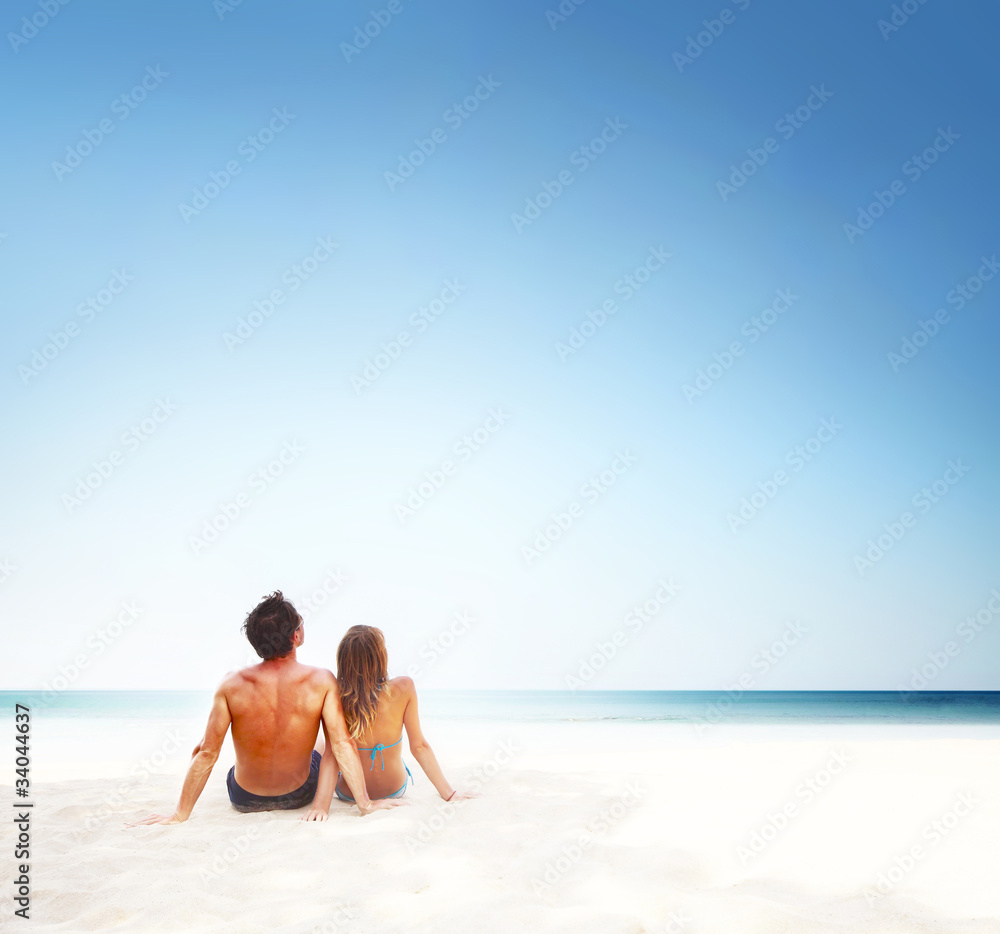Young couple sitting on the sand and looking to a blue tropical sky